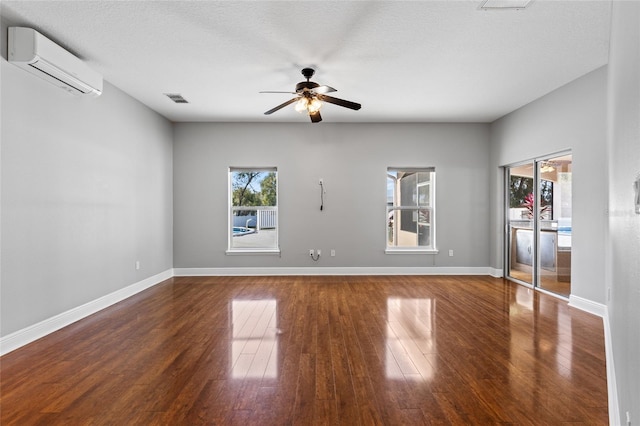 spare room with an AC wall unit, ceiling fan, dark wood-type flooring, and a textured ceiling