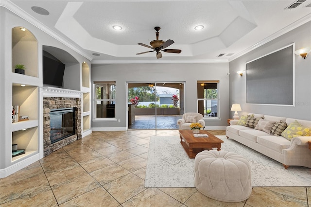 living room featuring a tray ceiling, a fireplace, ceiling fan, and built in features