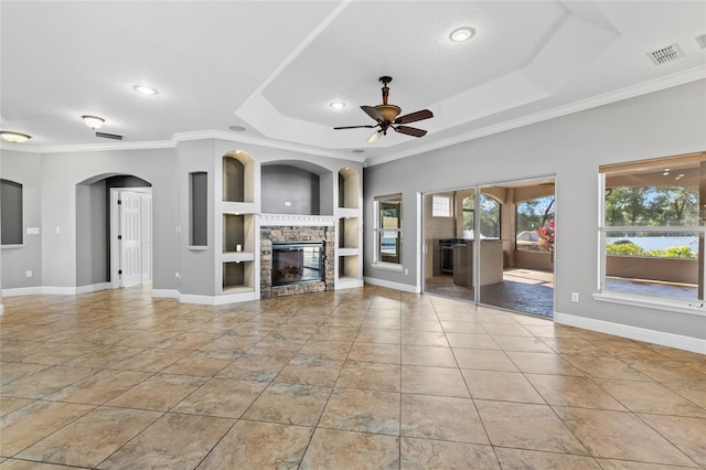 unfurnished living room with built in shelves, ornamental molding, a fireplace, and a tray ceiling