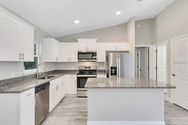 kitchen with white cabinetry, sink, stainless steel appliances, light stone counters, and a kitchen island