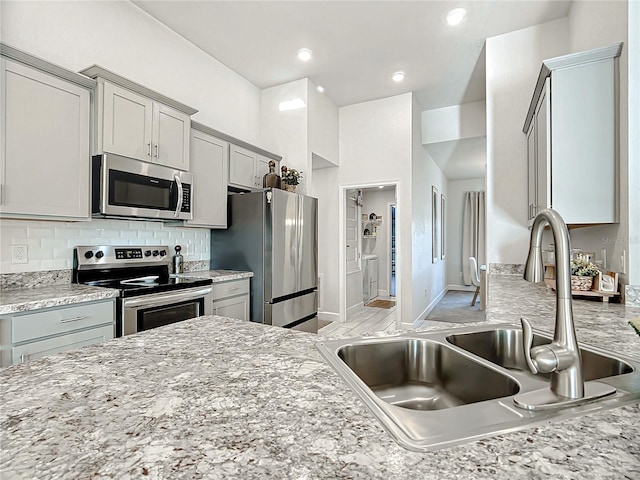 kitchen featuring gray cabinetry, light stone countertops, sink, stainless steel appliances, and tasteful backsplash