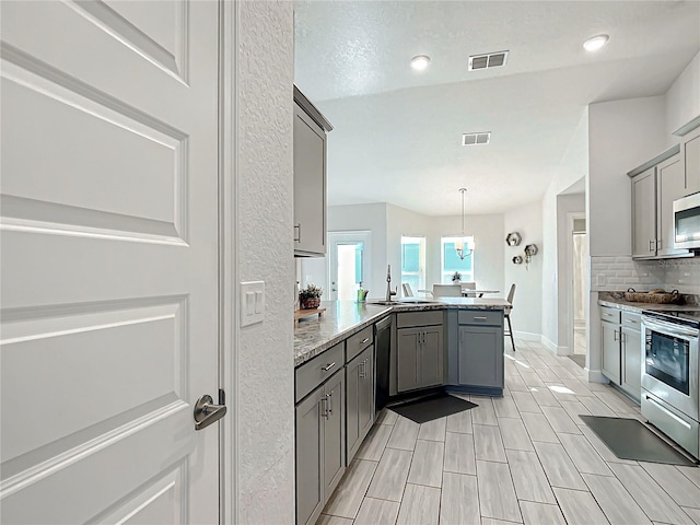 kitchen featuring kitchen peninsula, appliances with stainless steel finishes, gray cabinets, and pendant lighting