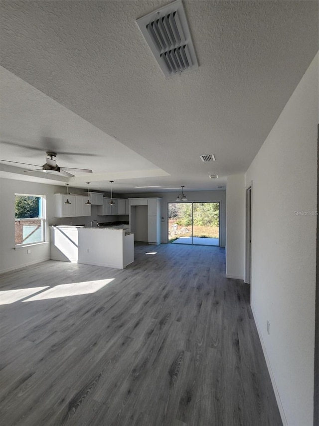 unfurnished living room featuring ceiling fan, dark wood-type flooring, and a textured ceiling