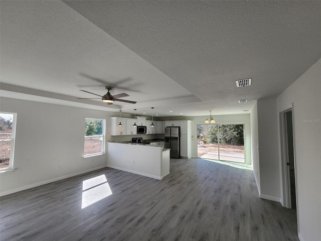 kitchen with appliances with stainless steel finishes, white cabinetry, hanging light fixtures, hardwood / wood-style floors, and kitchen peninsula