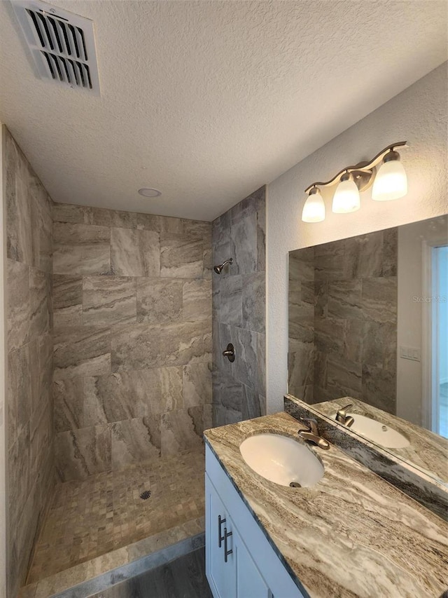 bathroom with vanity, a tile shower, and a textured ceiling