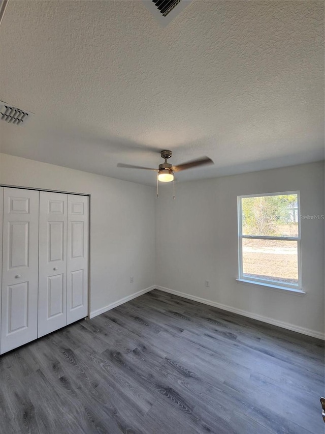 unfurnished bedroom with ceiling fan, dark hardwood / wood-style floors, a closet, and a textured ceiling