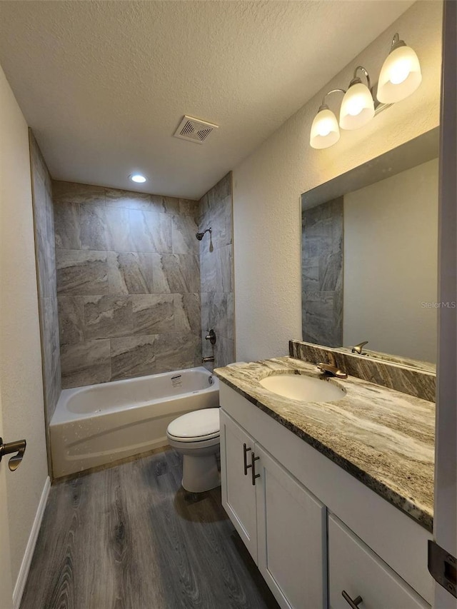 full bathroom with hardwood / wood-style floors, vanity, a textured ceiling, toilet, and tiled shower / bath