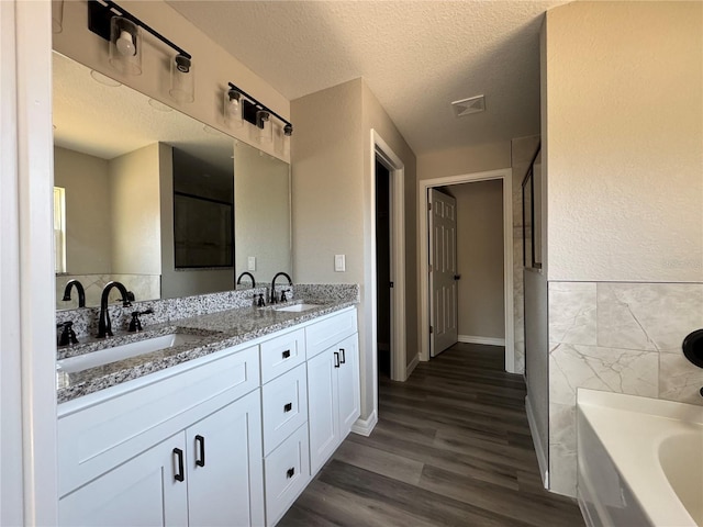 bathroom with vanity, wood-type flooring, a textured ceiling, and a tub to relax in