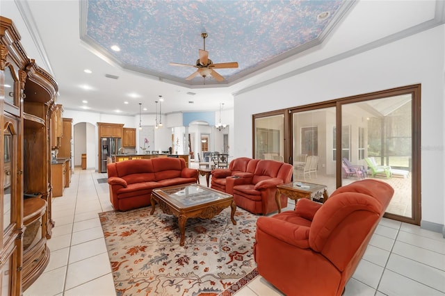 tiled living room with ceiling fan with notable chandelier, a raised ceiling, and crown molding