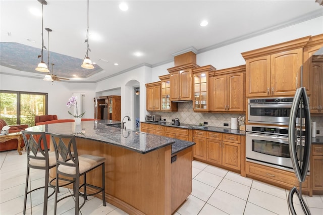 kitchen featuring ceiling fan, tasteful backsplash, crown molding, pendant lighting, and a center island with sink