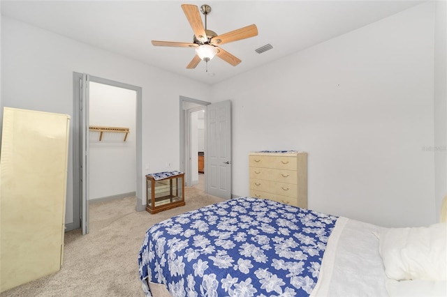 bedroom featuring ceiling fan, a walk in closet, and light carpet