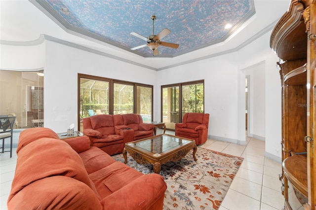 living room with a high ceiling, a raised ceiling, crown molding, ceiling fan, and light tile patterned floors