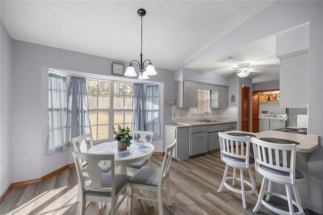 dining space with light wood-type flooring, ceiling fan with notable chandelier, a textured ceiling, sink, and separate washer and dryer