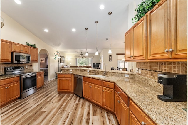 kitchen with kitchen peninsula, light stone countertops, stainless steel appliances, sink, and decorative light fixtures