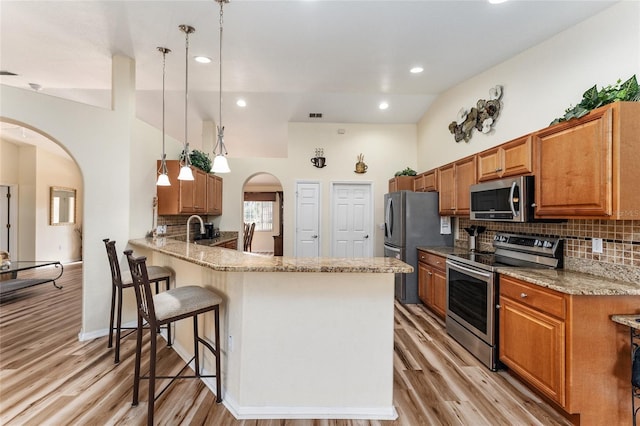 kitchen with hanging light fixtures, vaulted ceiling, light stone countertops, kitchen peninsula, and stainless steel appliances