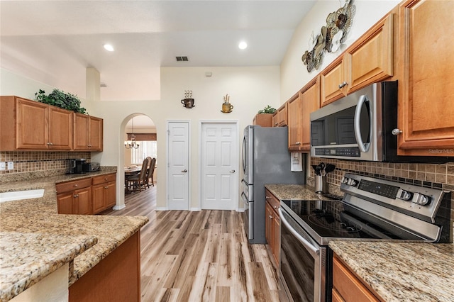 kitchen with light hardwood / wood-style flooring, decorative backsplash, appliances with stainless steel finishes, a notable chandelier, and light stone counters