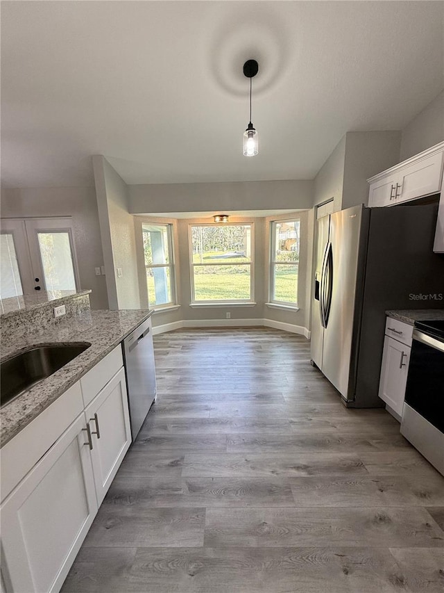 kitchen with light stone countertops, appliances with stainless steel finishes, white cabinetry, and hanging light fixtures