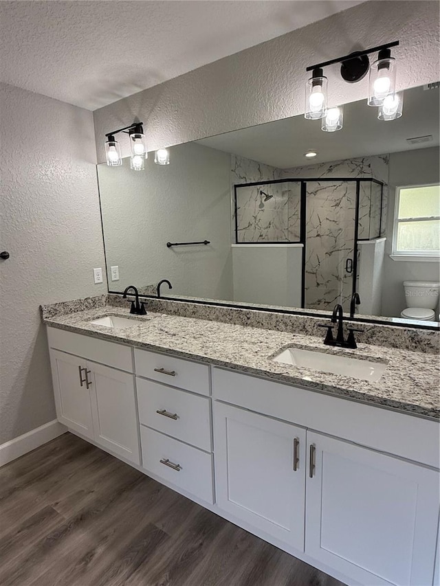 bathroom featuring hardwood / wood-style floors, a textured ceiling, toilet, vanity, and a shower with shower door