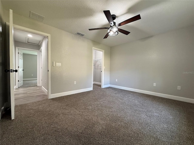 unfurnished bedroom featuring a walk in closet, a textured ceiling, ceiling fan, carpet floors, and a closet