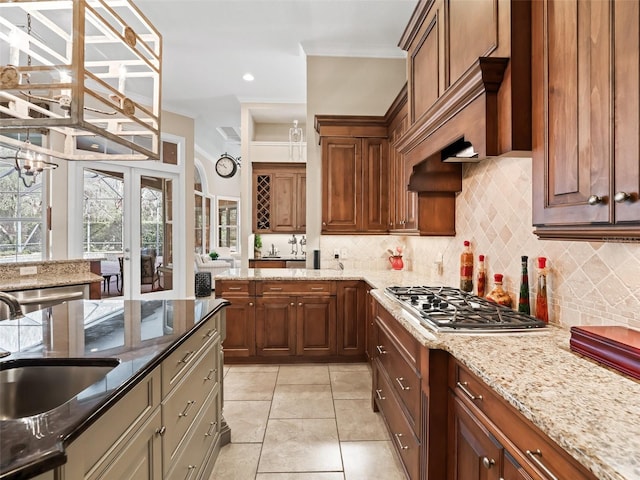 kitchen featuring sink, stainless steel gas cooktop, tasteful backsplash, light stone counters, and light tile patterned floors