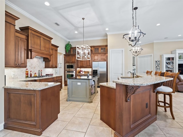 kitchen featuring appliances with stainless steel finishes, decorative light fixtures, light stone counters, and a large island with sink