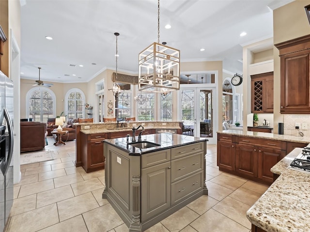 kitchen with a center island with sink, ceiling fan with notable chandelier, sink, hanging light fixtures, and light stone countertops