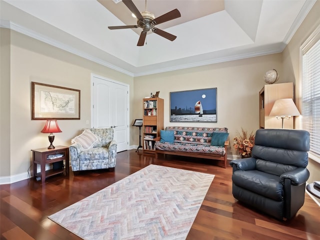 living room with a tray ceiling, ceiling fan, dark wood-type flooring, and ornamental molding