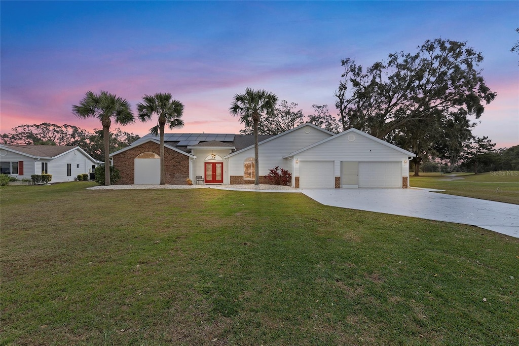 single story home featuring solar panels, a yard, and a garage