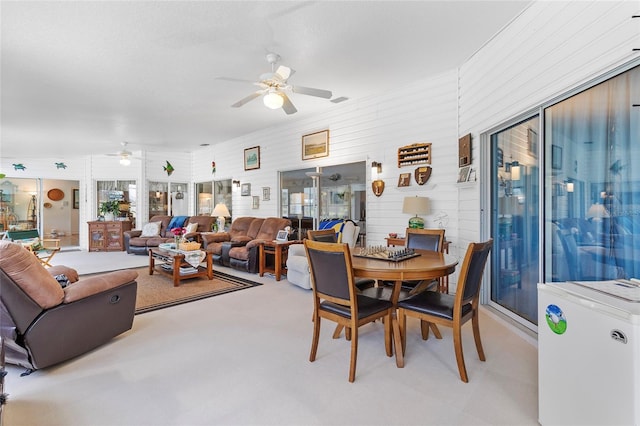 dining space with ceiling fan, light colored carpet, and wooden walls