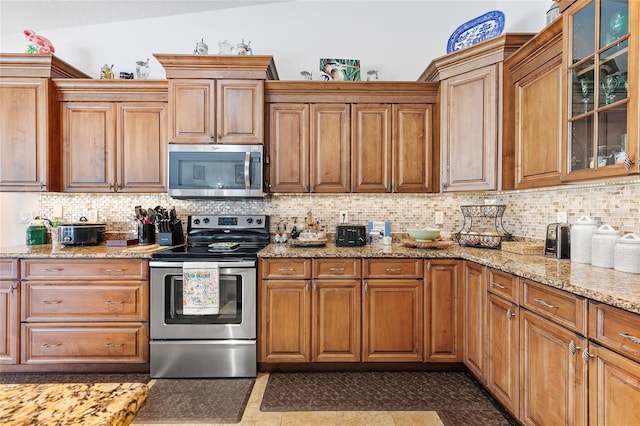 kitchen featuring tasteful backsplash, light stone counters, vaulted ceiling, and appliances with stainless steel finishes