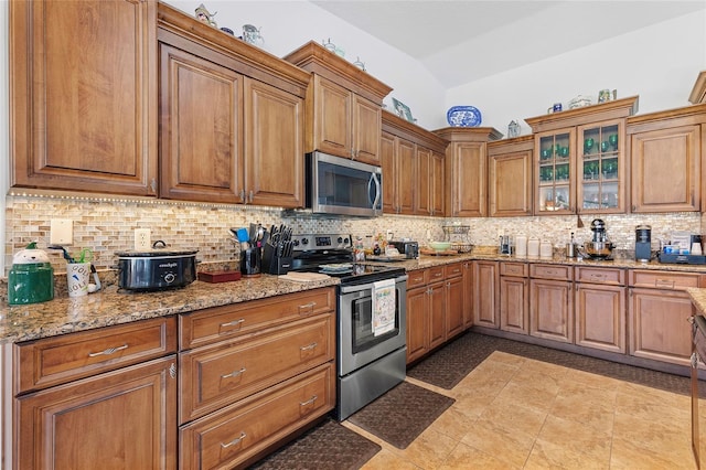 kitchen featuring vaulted ceiling, light stone countertops, tasteful backsplash, light tile patterned flooring, and stainless steel appliances