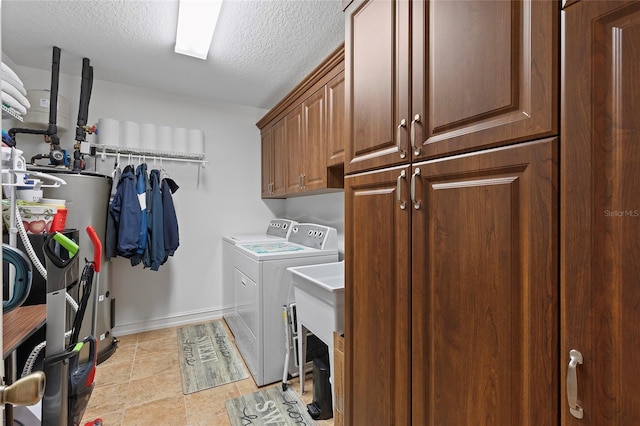 clothes washing area with cabinets, a textured ceiling, water heater, and washing machine and clothes dryer