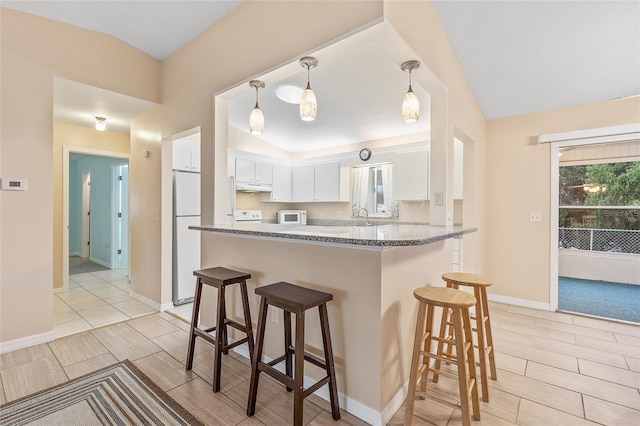 kitchen featuring kitchen peninsula, white appliances, dark stone countertops, white cabinets, and a breakfast bar area