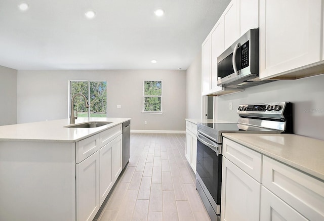 kitchen with appliances with stainless steel finishes, sink, a center island with sink, light hardwood / wood-style flooring, and white cabinets