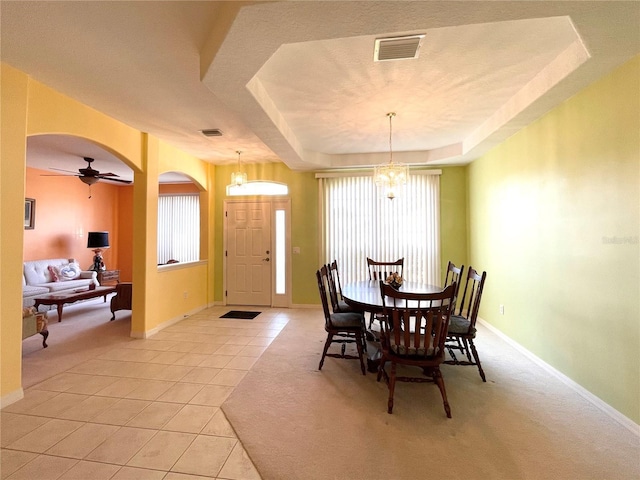 tiled dining area with a raised ceiling and ceiling fan with notable chandelier