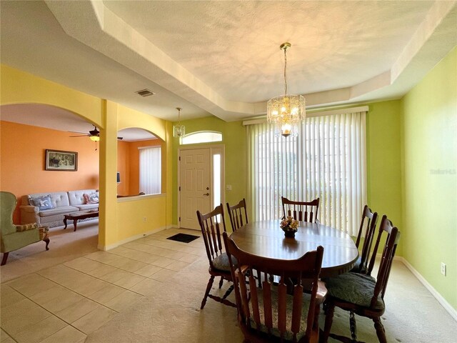 tiled dining space with a tray ceiling, a textured ceiling, and ceiling fan with notable chandelier