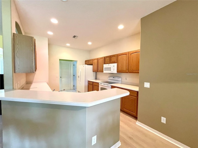 kitchen with kitchen peninsula, white appliances, and light hardwood / wood-style floors