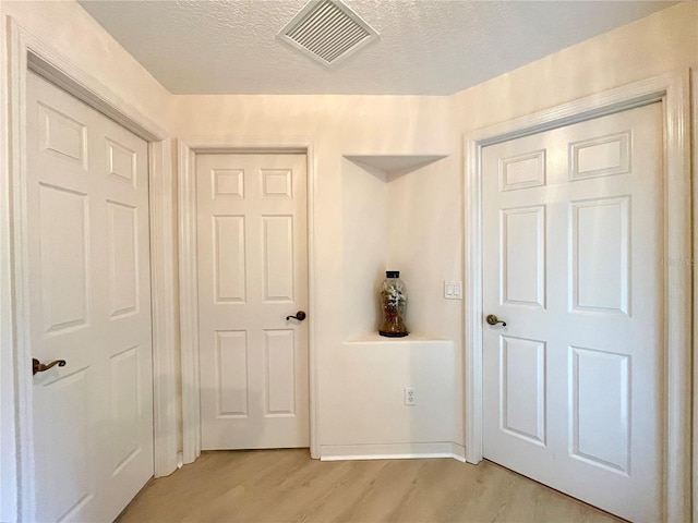 corridor with light hardwood / wood-style floors and a textured ceiling