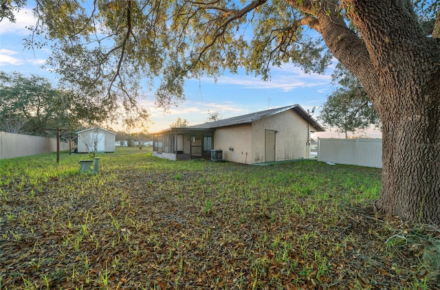 yard at dusk featuring central air condition unit and a storage shed