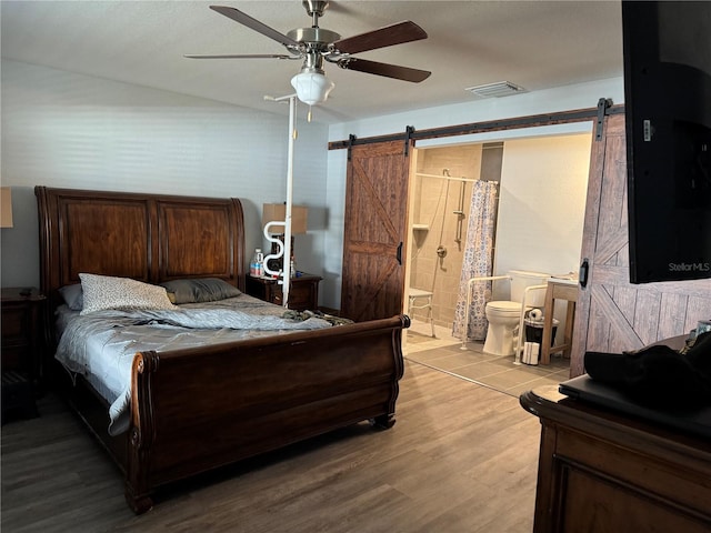 bedroom with light wood-type flooring, a barn door, ensuite bathroom, and ceiling fan