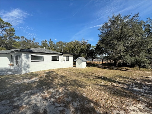 view of home's exterior featuring a shed, concrete block siding, a lawn, and an outdoor structure