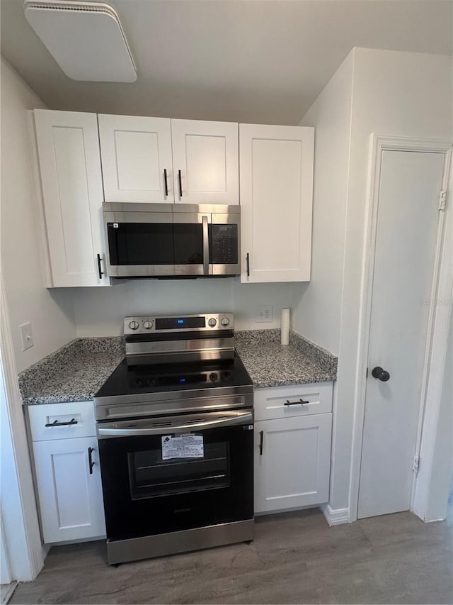 kitchen with stone counters, appliances with stainless steel finishes, white cabinets, and wood finished floors