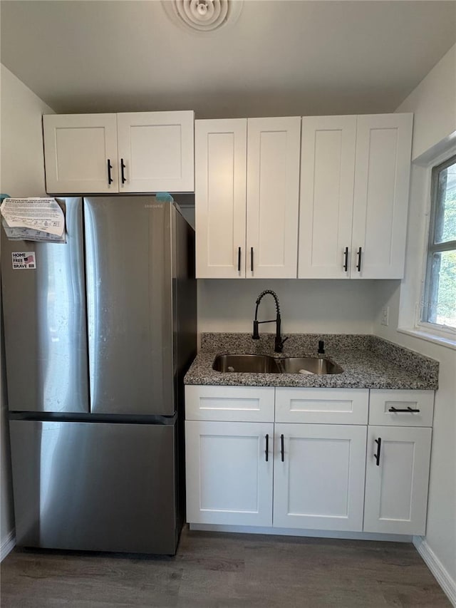 kitchen with dark stone counters, a sink, freestanding refrigerator, and white cabinets