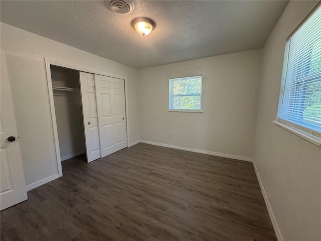 unfurnished bedroom with a textured ceiling, dark hardwood / wood-style floors, and a closet