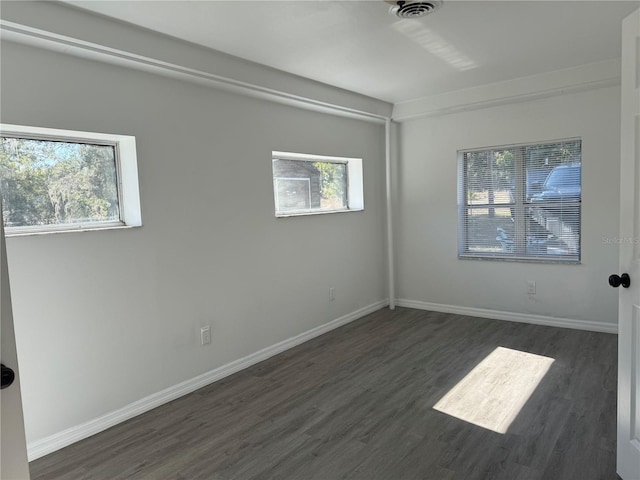 empty room with dark wood-type flooring, visible vents, and baseboards