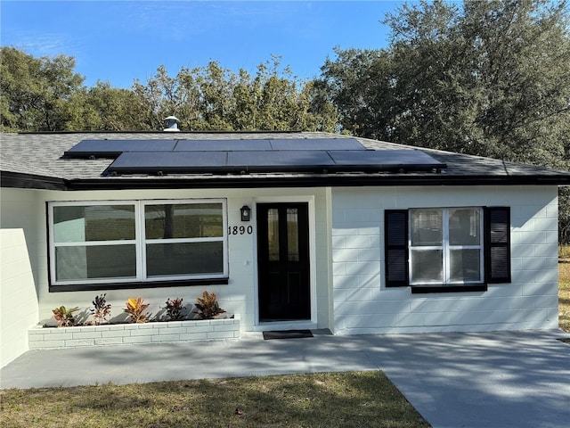 view of front facade with concrete block siding, roof with shingles, and solar panels