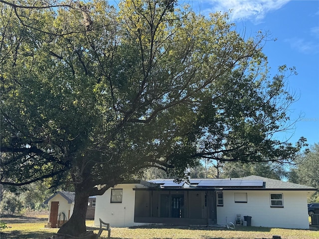 back of property featuring a lawn, a shed, and solar panels