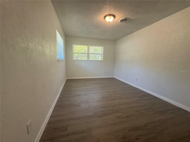 unfurnished room with a textured ceiling, a textured wall, dark wood-style flooring, visible vents, and baseboards