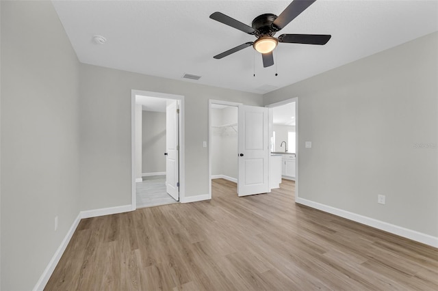 unfurnished bedroom featuring ceiling fan, sink, light hardwood / wood-style floors, a walk in closet, and a closet