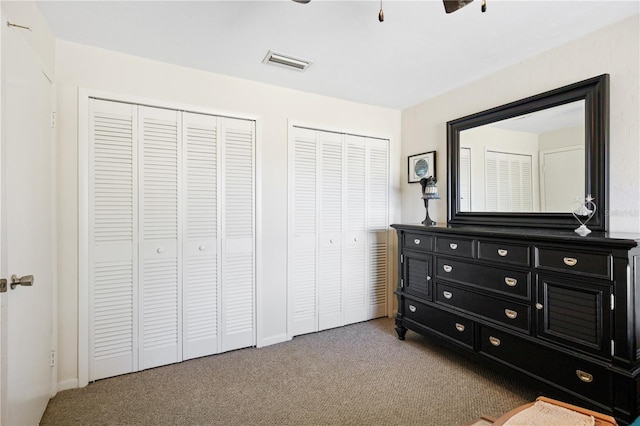 carpeted bedroom with ceiling fan and multiple closets